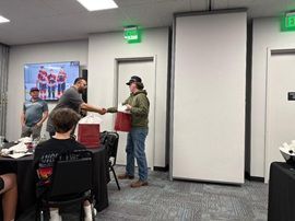 People exchanging a handshake in a conference room with seated attendees and a projector screen.