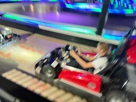 Child driving a red bumper car on an indoor track with colorful lights nearby