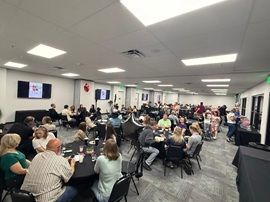 Conference room with many people seated at round tables, watching a presentation on a wall screen