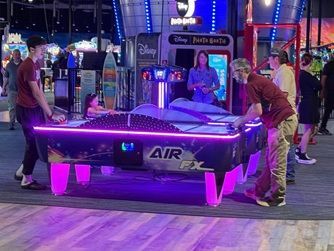 Two men showcasing a glowing purple air hockey table at a carnival booth