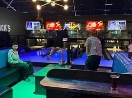 People at neon-lit bowling lanes with green benches and arcade screens in the background