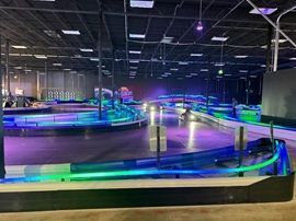Indoor go-kart track with glowing blue and purple LED lights and curved barriers