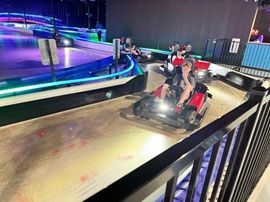 People driving go-karts on an indoor track with neon blue and purple lighting