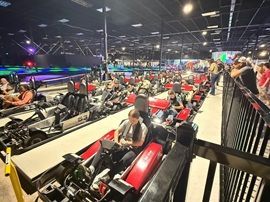 Indoor go-kart track with rows of red and black karts and people waiting in the stands