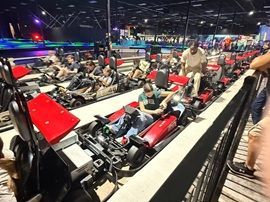 People riding go-karts on a brightly lit indoor track with red-and-black vehicles