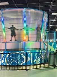 Kids bouncing on an illuminated indoor circular ride behind a black fence