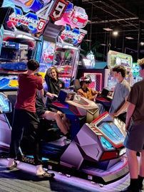 People playing a neon racing arcade game in a dimly lit arcade.