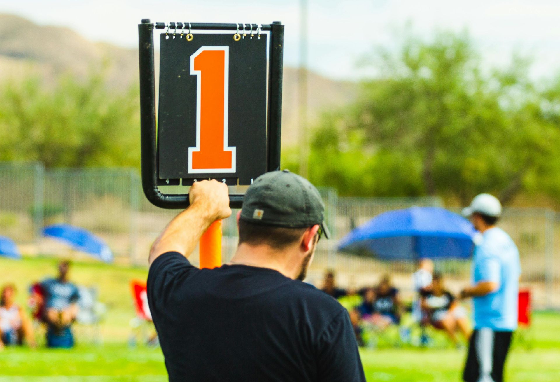 Person holding up a black sign with a large orange “1” at a sports field event
