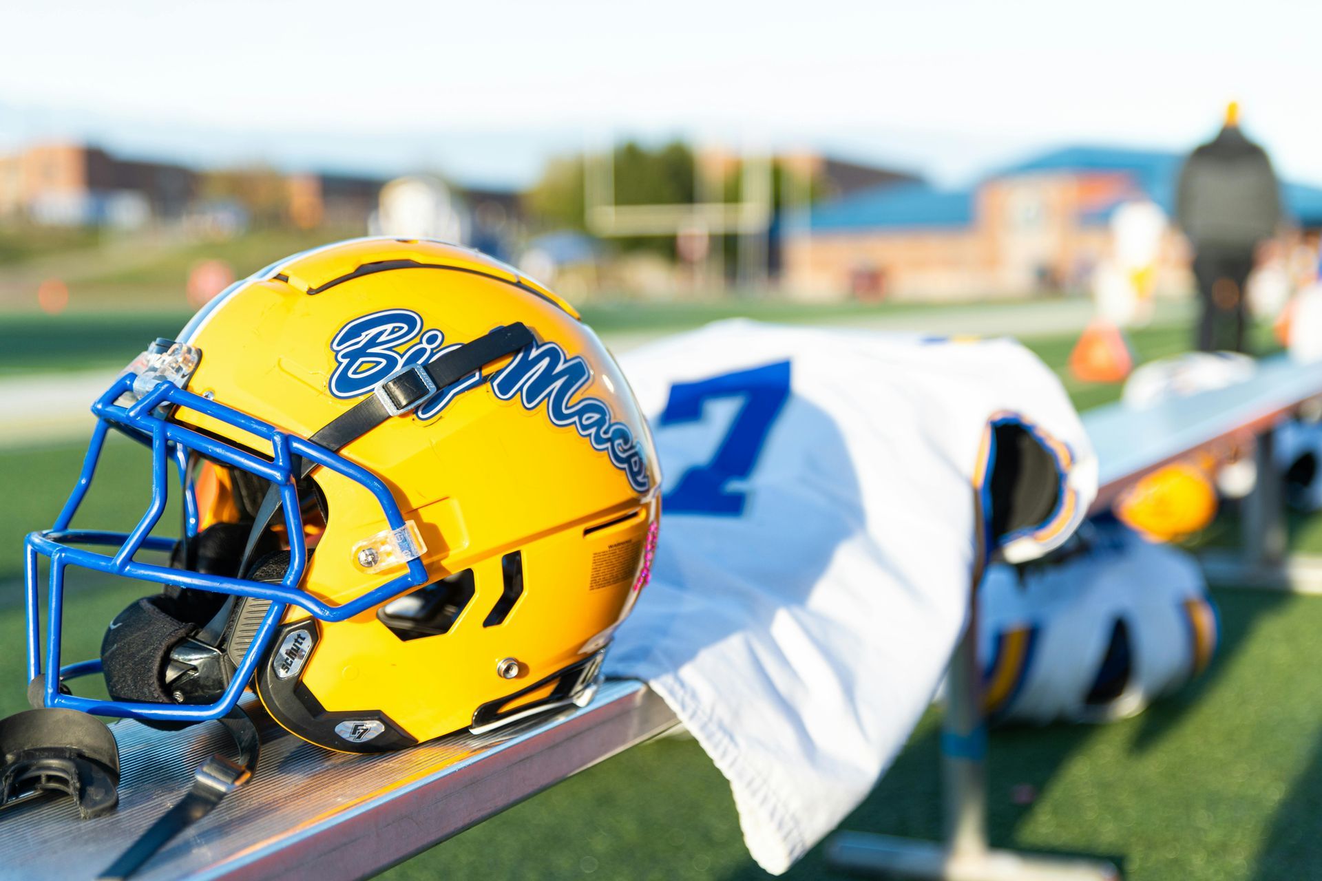 Yellow football helmet and white jersey draped over a sideline railing on a field