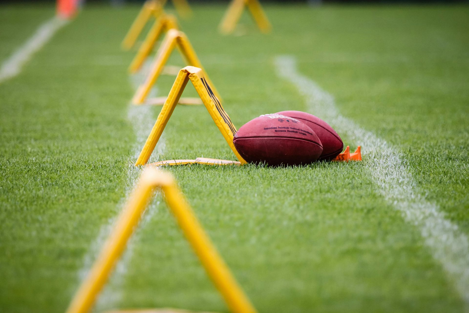 Football on a practice field beside yellow training cones and a sideline marker