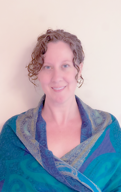 Person smiling in a teal and blue patterned wrap against a plain light background