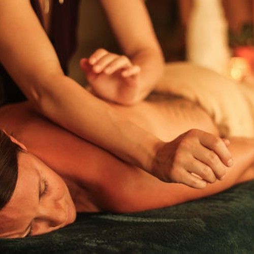 A person receiving a back massage with folded towels in warm, dim lighting