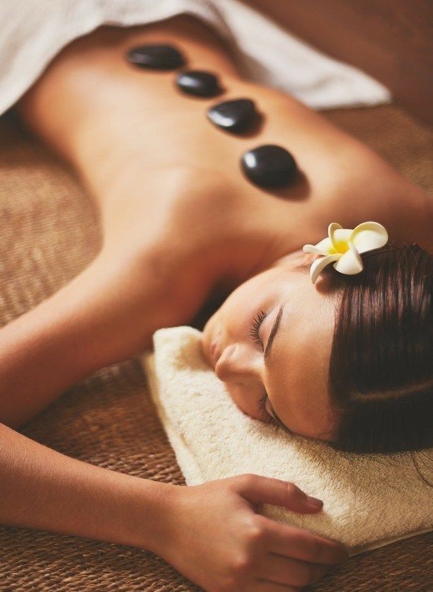 Spa massage with woman lying face down, hot stones on her back, and a flower in her hair