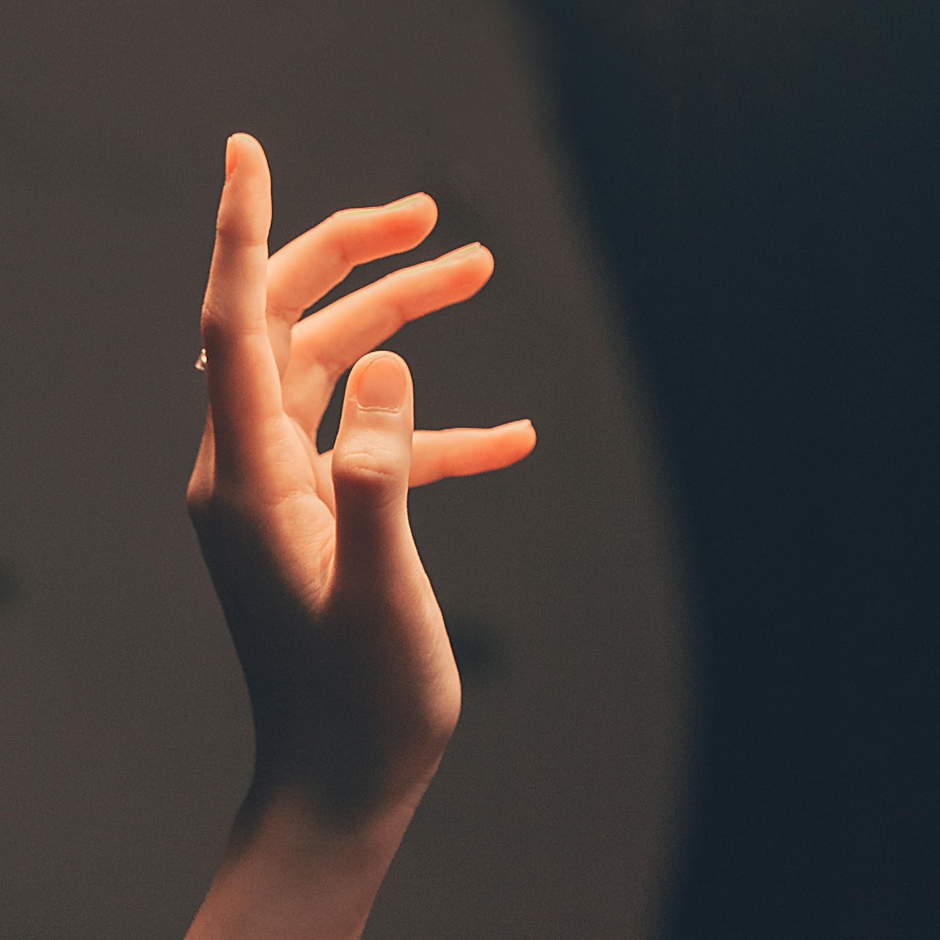 Two hands reaching toward each other in warm, soft light against a dark background