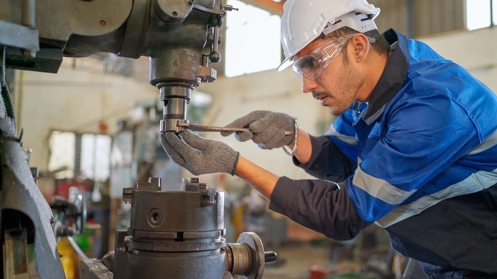Engineer in safety gear using a wrench to repair industrial machinery