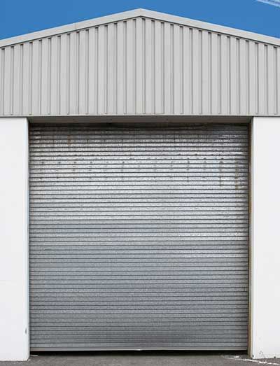 Un edificio blanco con una puerta de garaje metálica y un cielo azul de fondo.