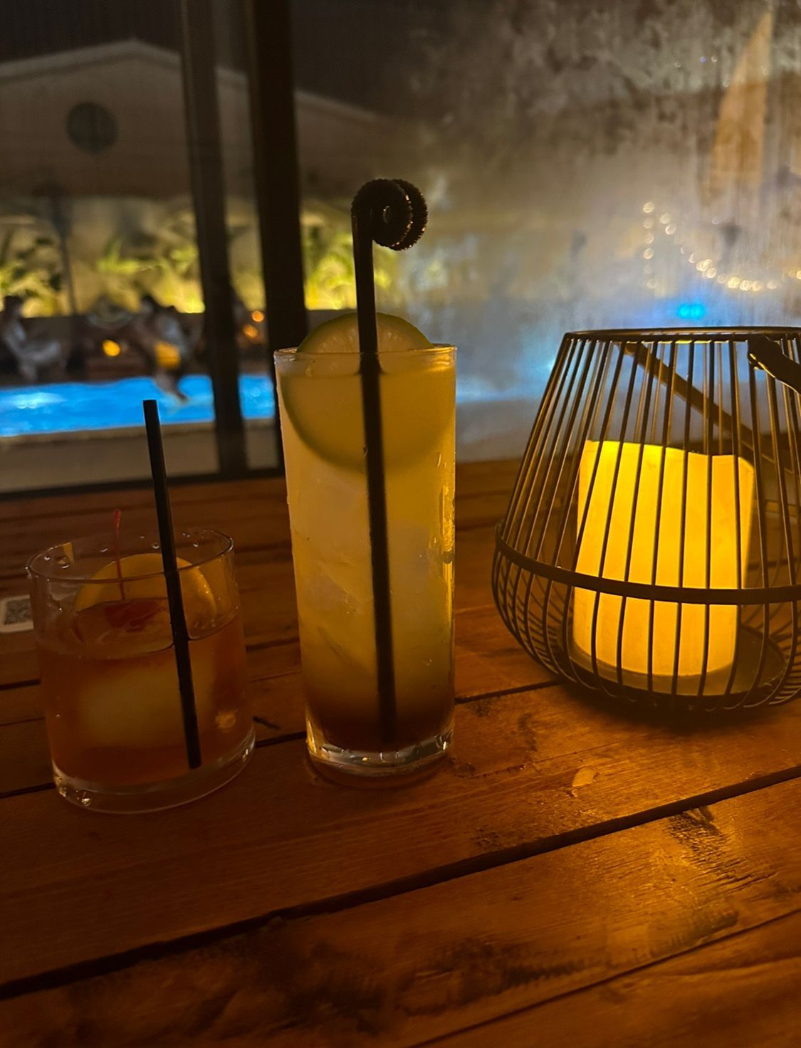 Two drinks are sitting on a wooden table next to a candle.