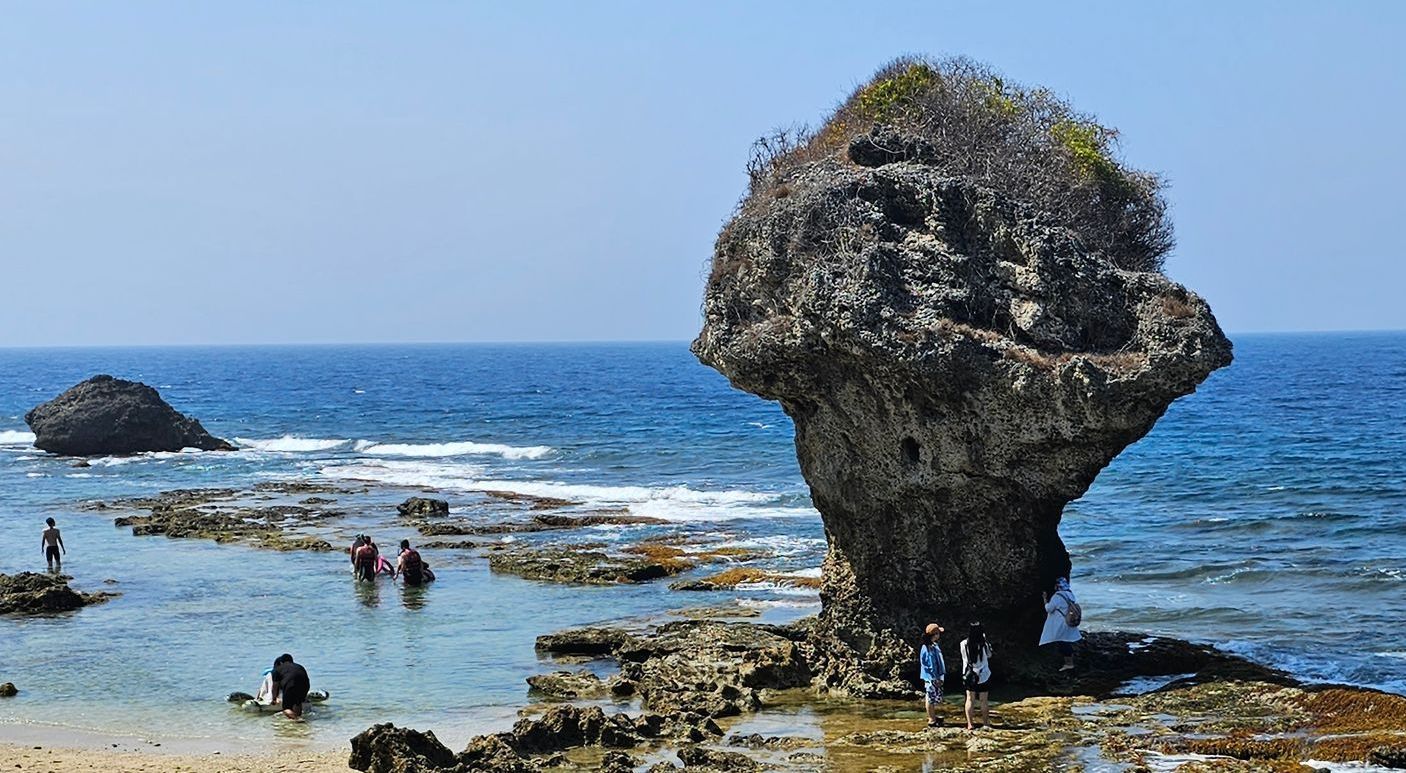 A group of people are standing on a rocky beach near the ocean.