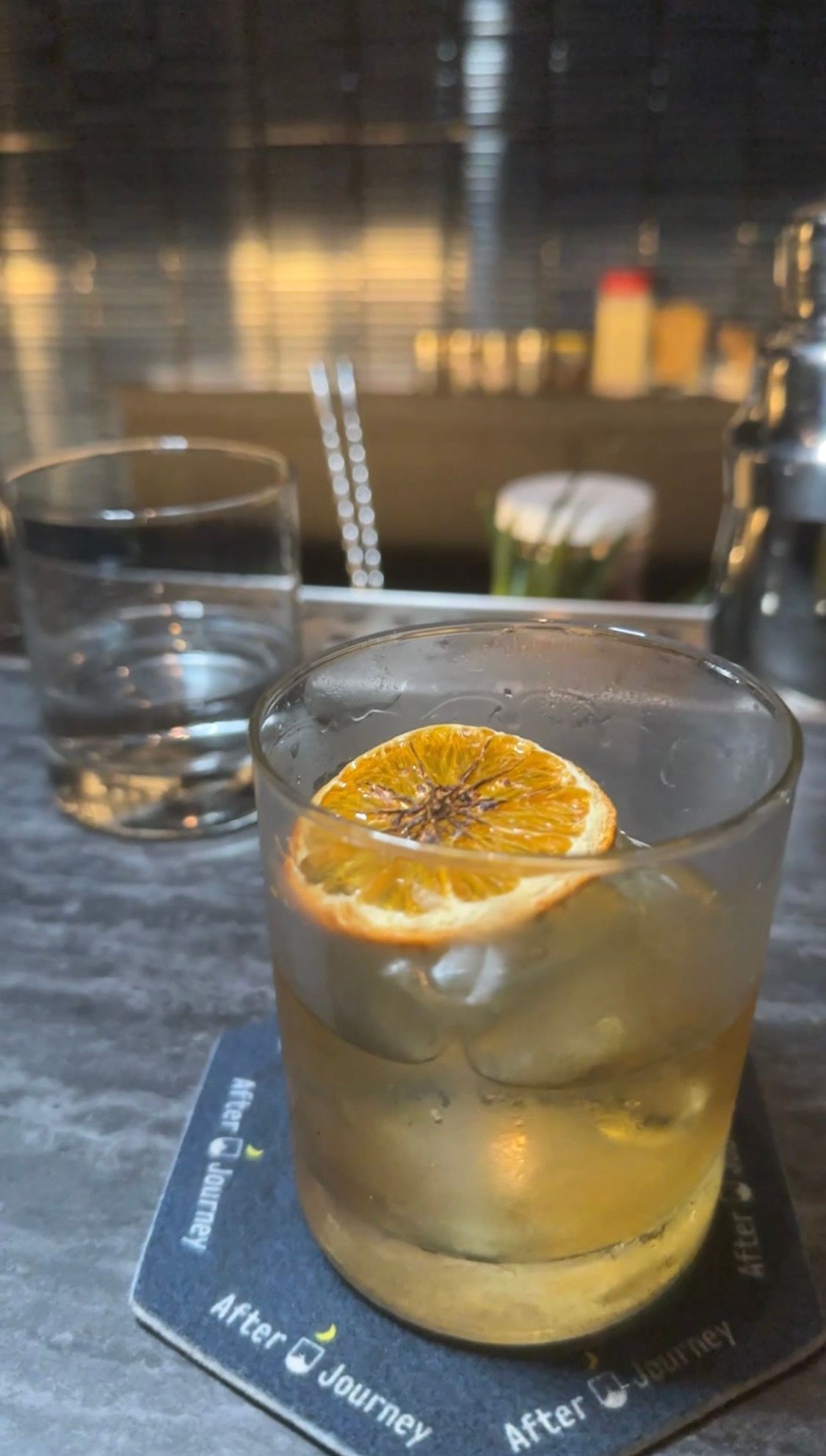 A glass of whiskey with an orange slice on top is on a coaster.