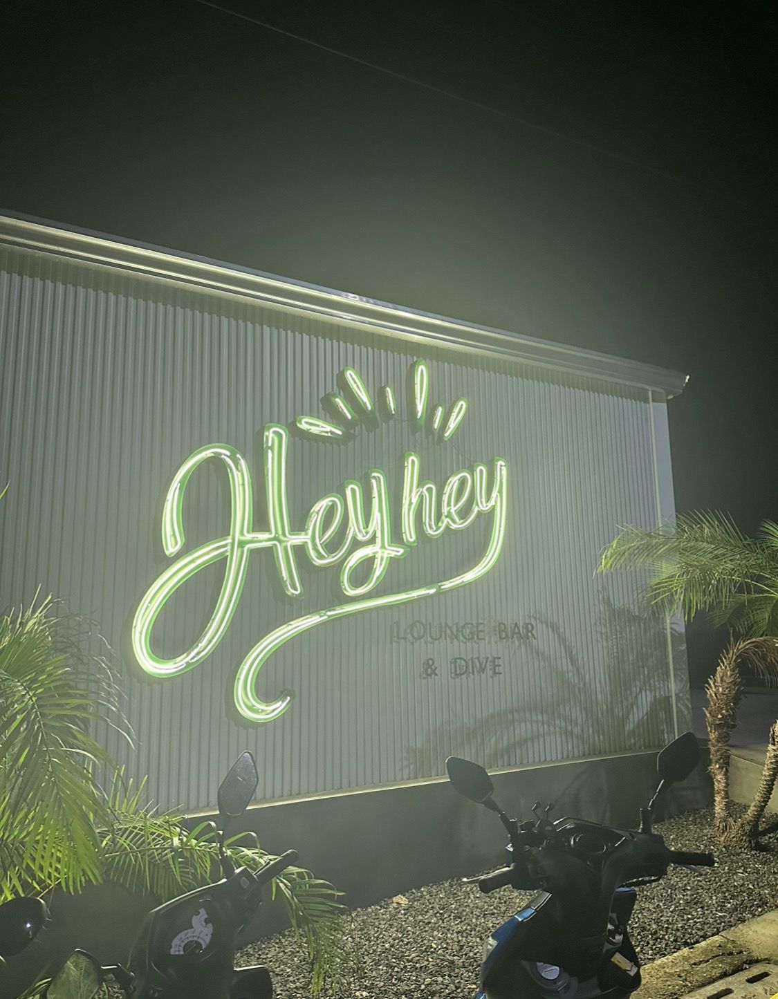 A motorcycle is parked in front of a building with a neon sign that says hey hey.