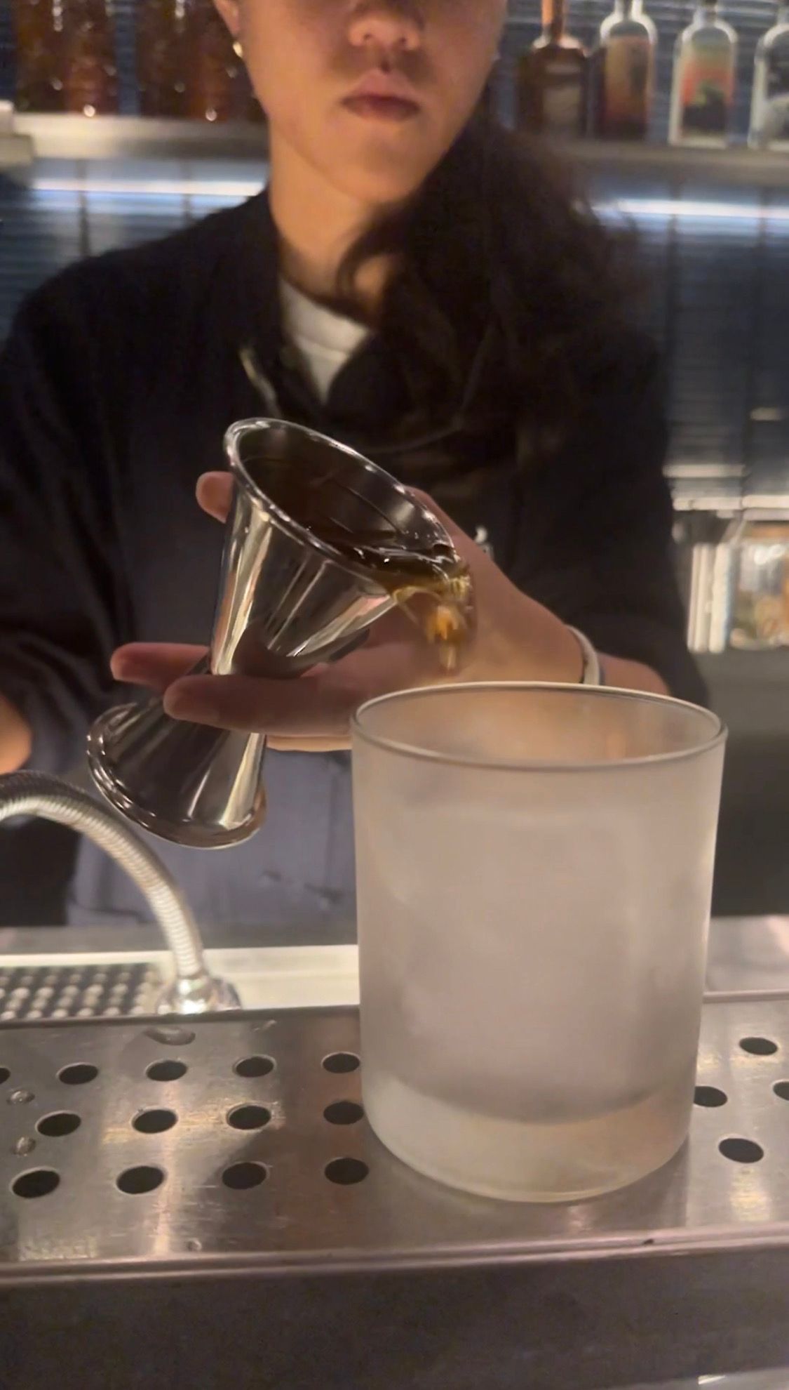 A bartender is holding a measuring cup and pouring liquid into a glass.