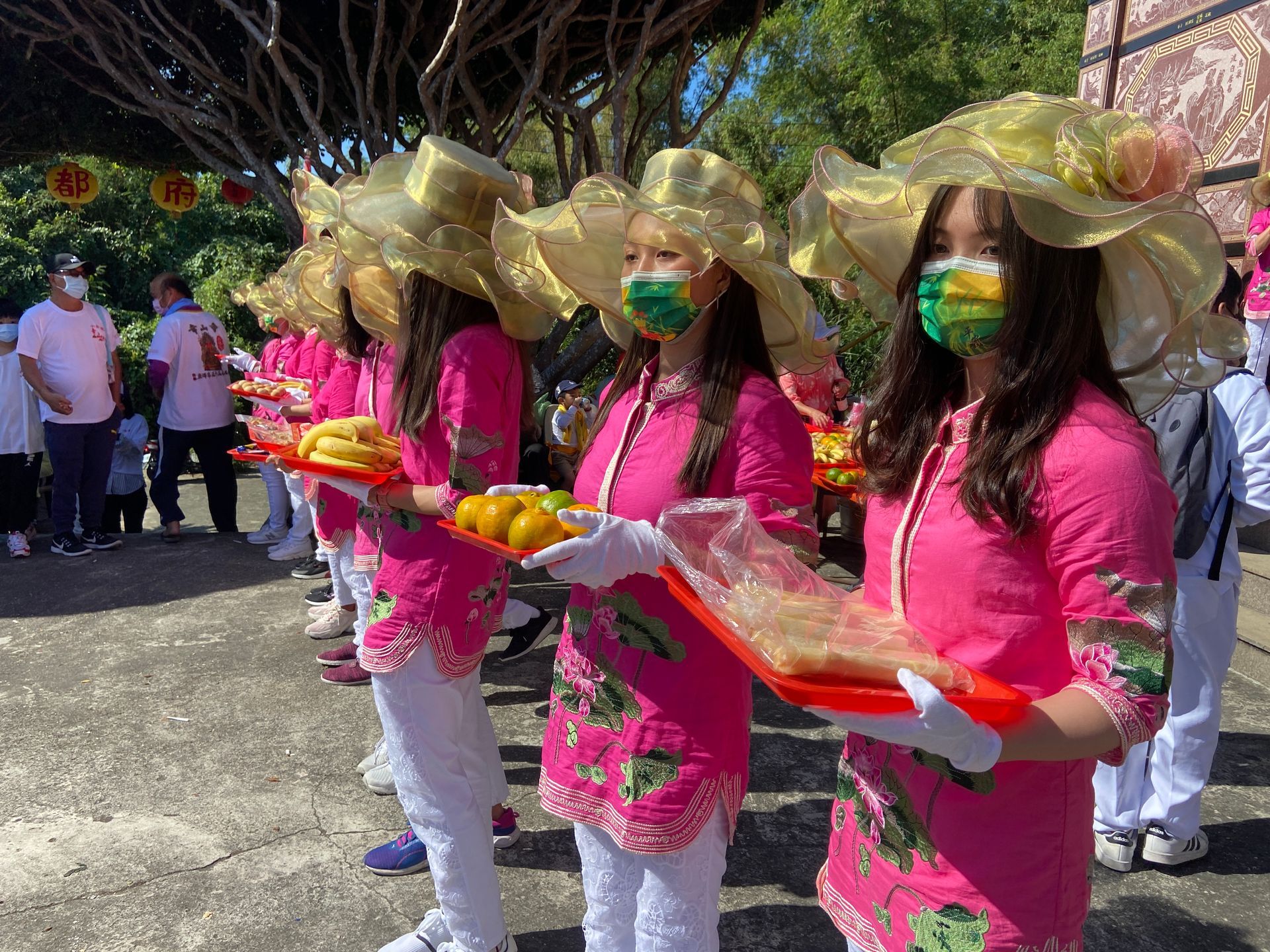 A group of women wearing masks and hats are holding trays of food.