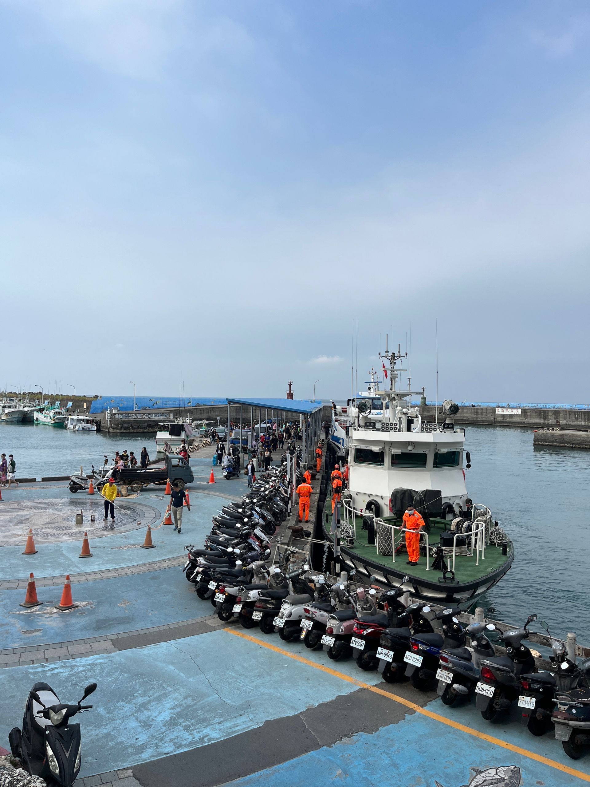 A row of motorcycles are parked in front of a boat in a harbor.