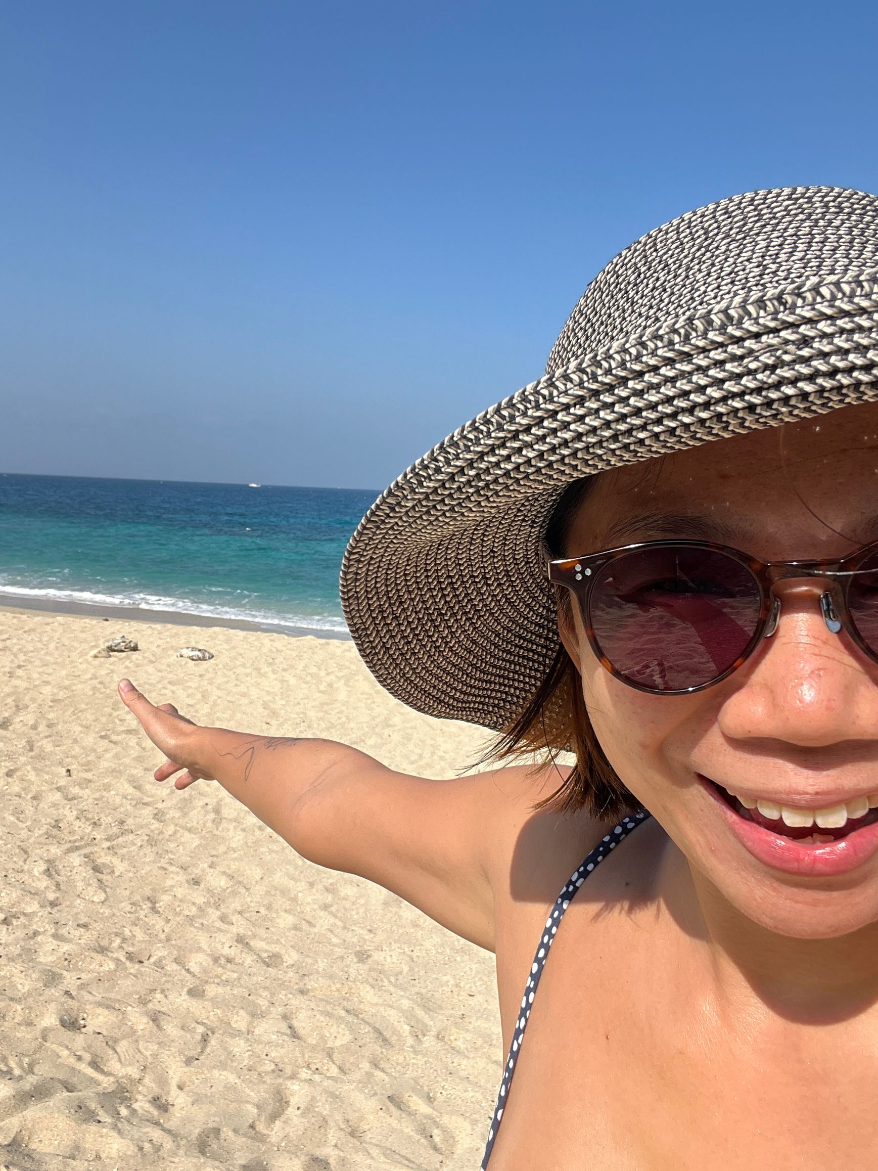 A woman wearing a hat and sunglasses is standing on a beach