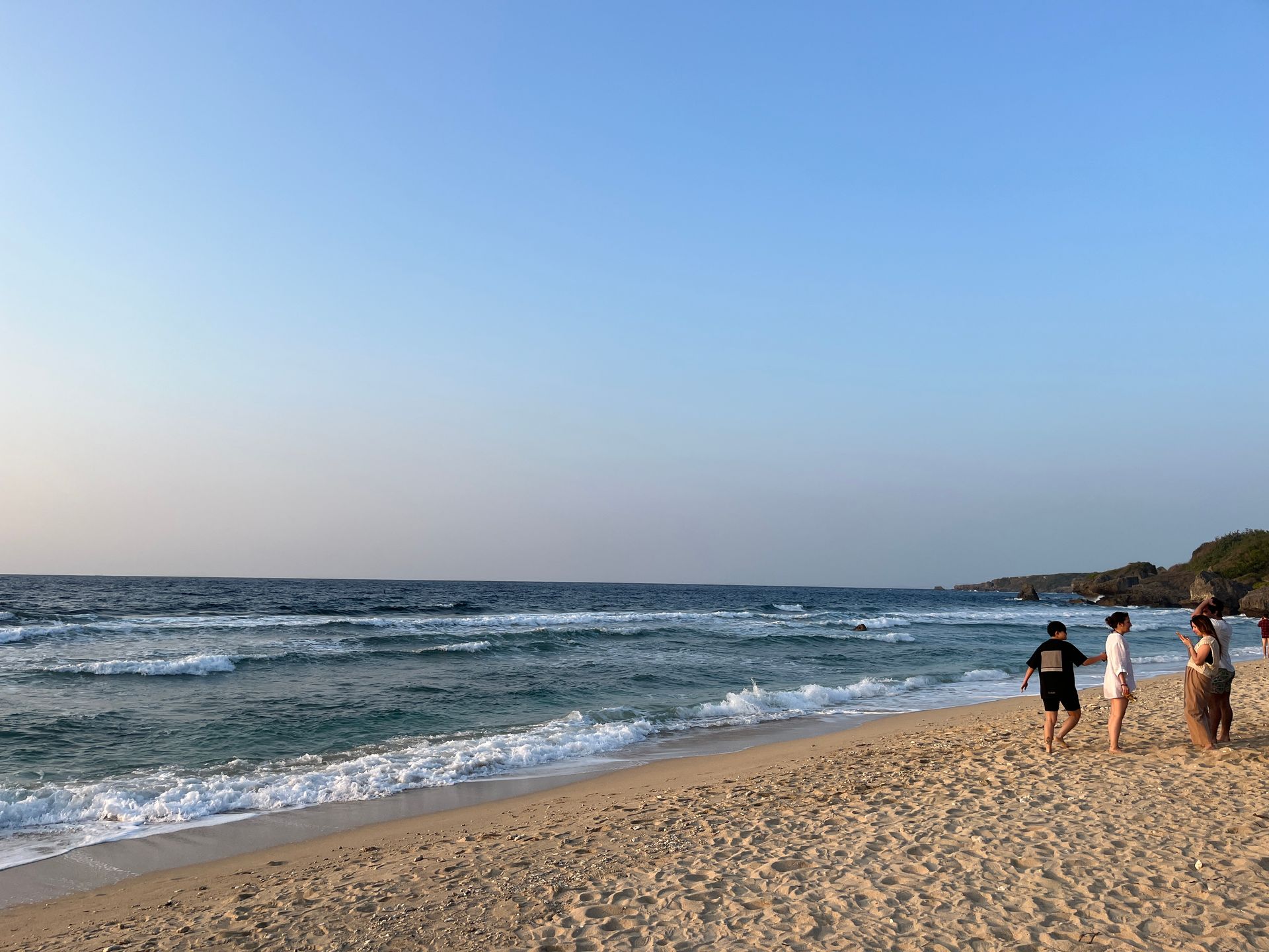 A group of people are standing on a beach looking at the ocean.