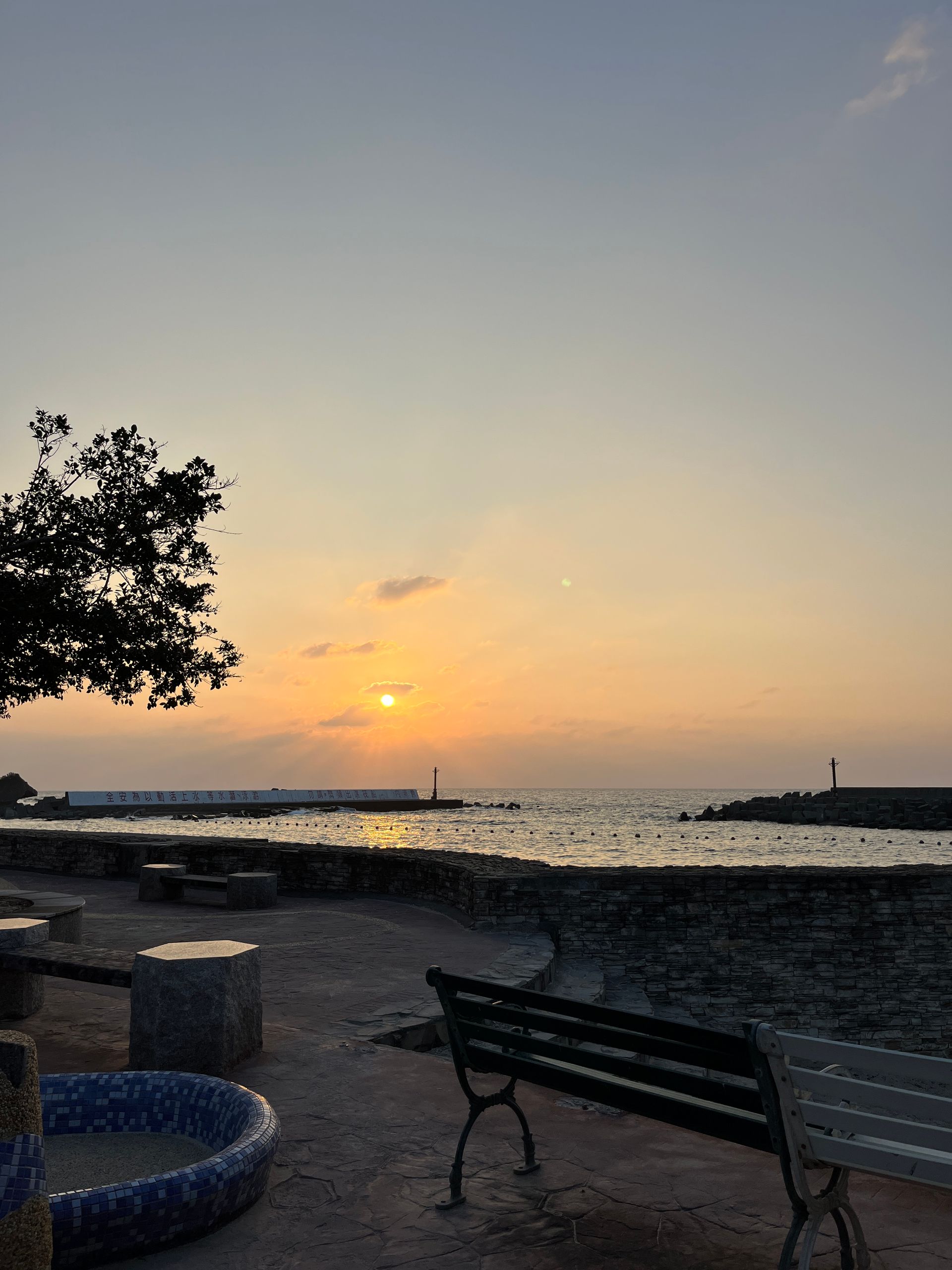 A sunset over the ocean with a bench in the foreground