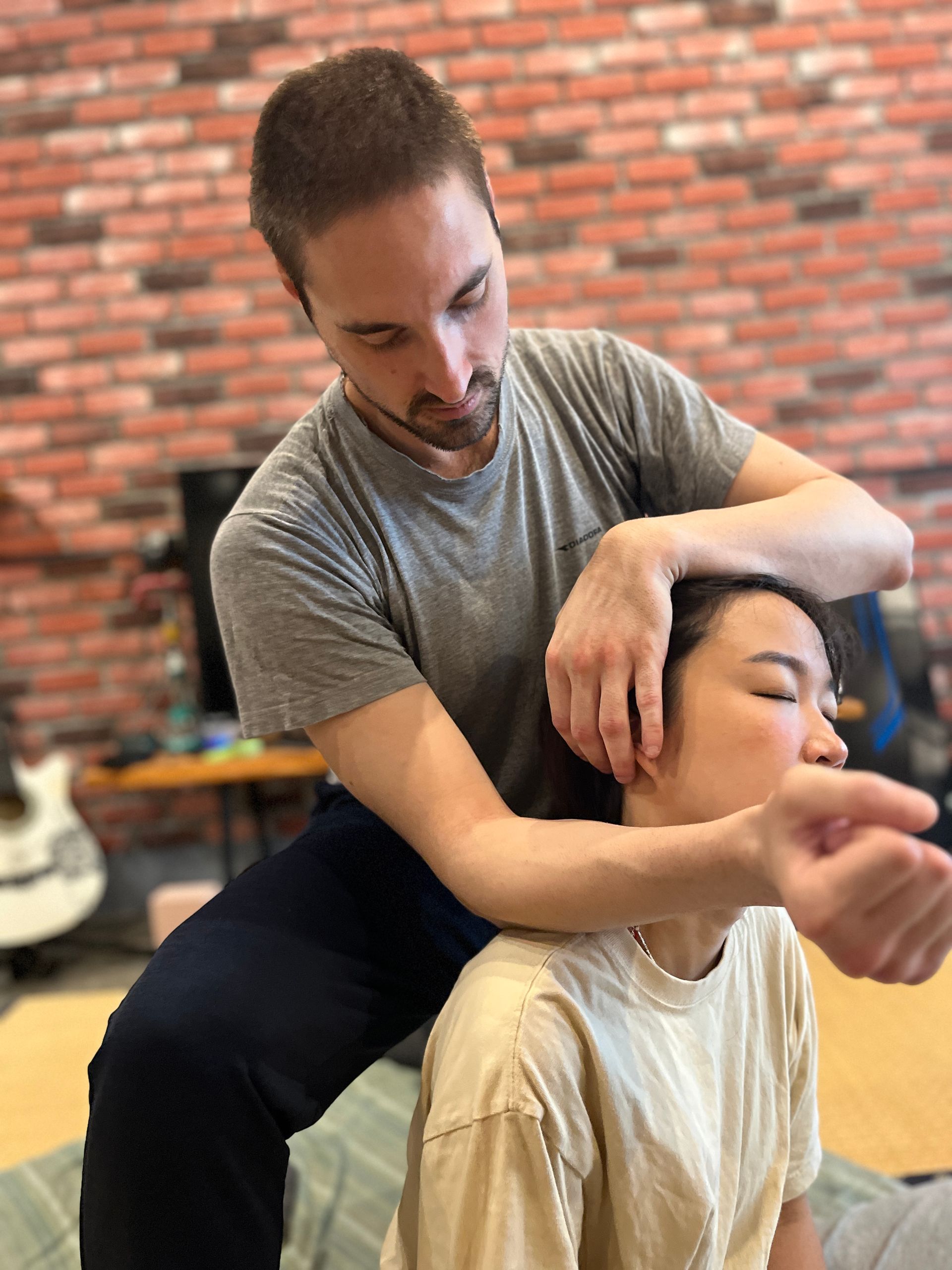 A man is giving a woman a massage in front of a brick wall.