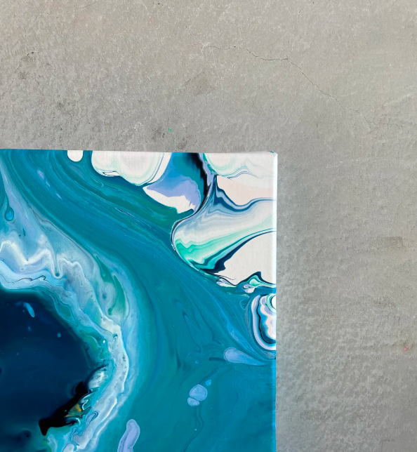 A person is pouring paint into a cup on a canvas.