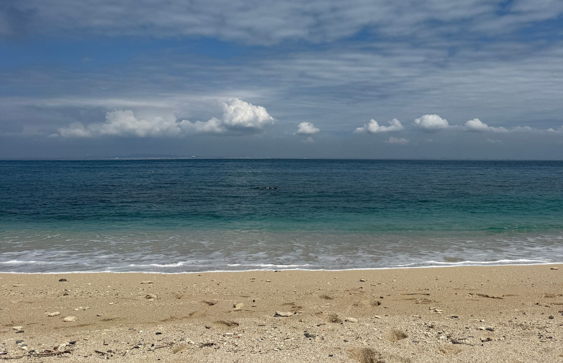 Sandy beach with calm blue ocean and cloudy sky on the horizon
