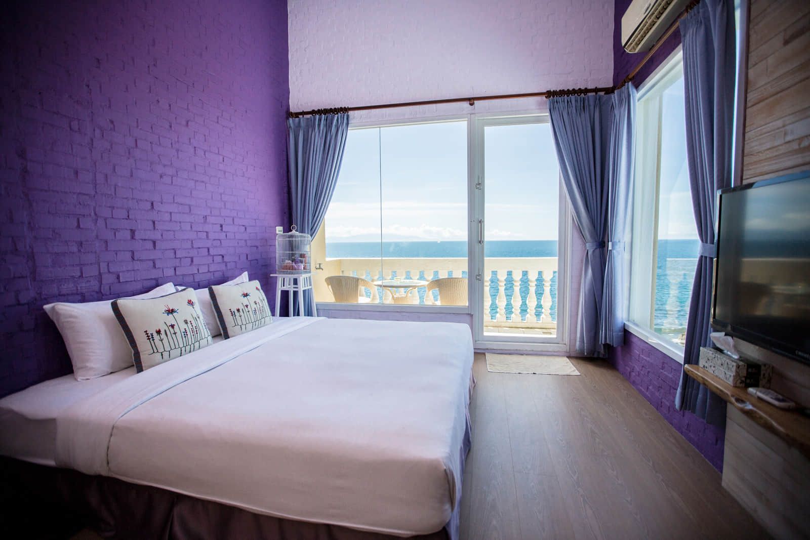 A bedroom with purple walls and a large bed with a view of the ocean.