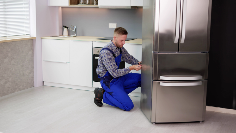 A man is kneeling down in front of a refrigerator in a kitchen.