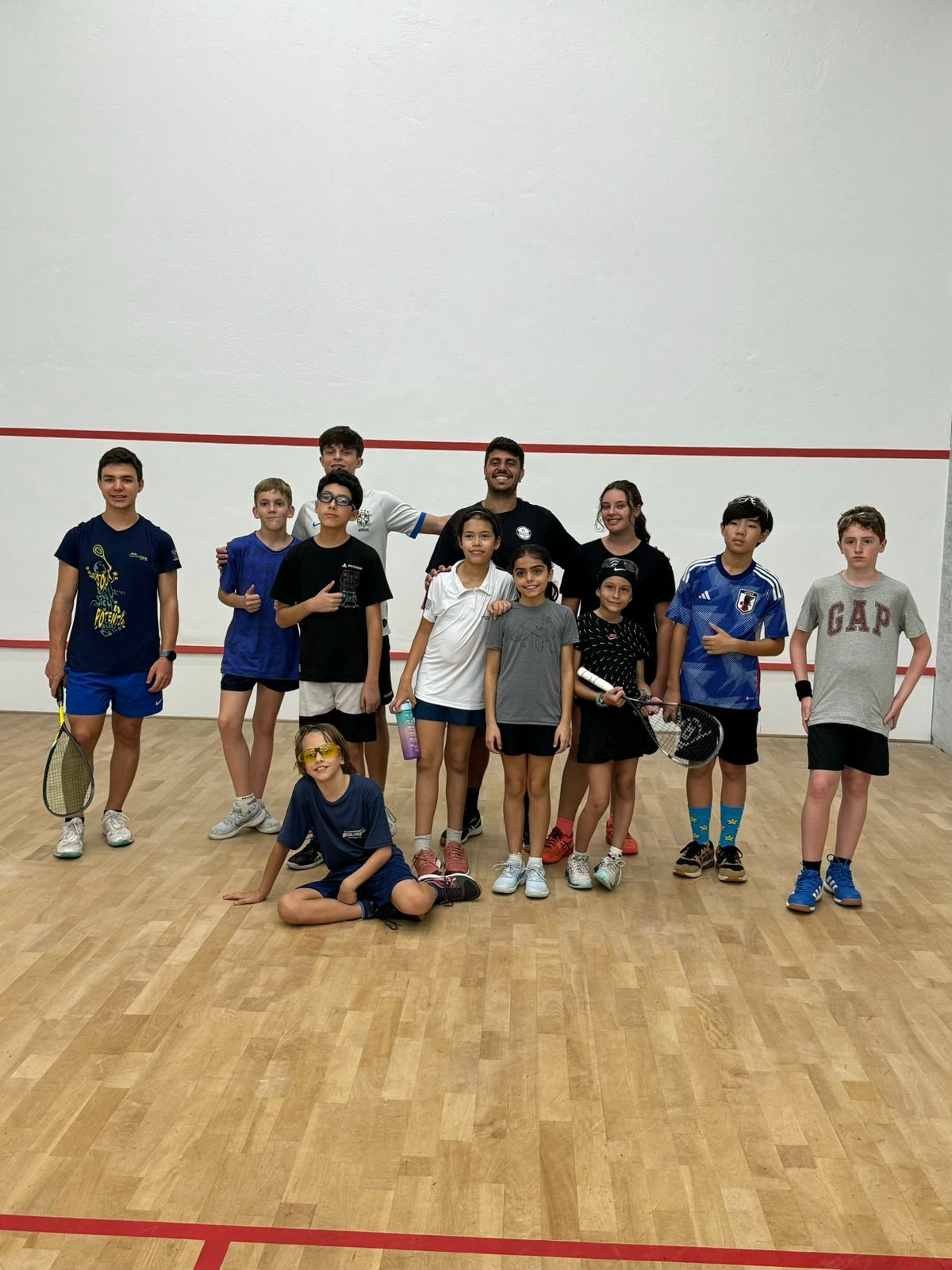 Um grupo de jovens está posando para uma foto em uma quadra de squash.