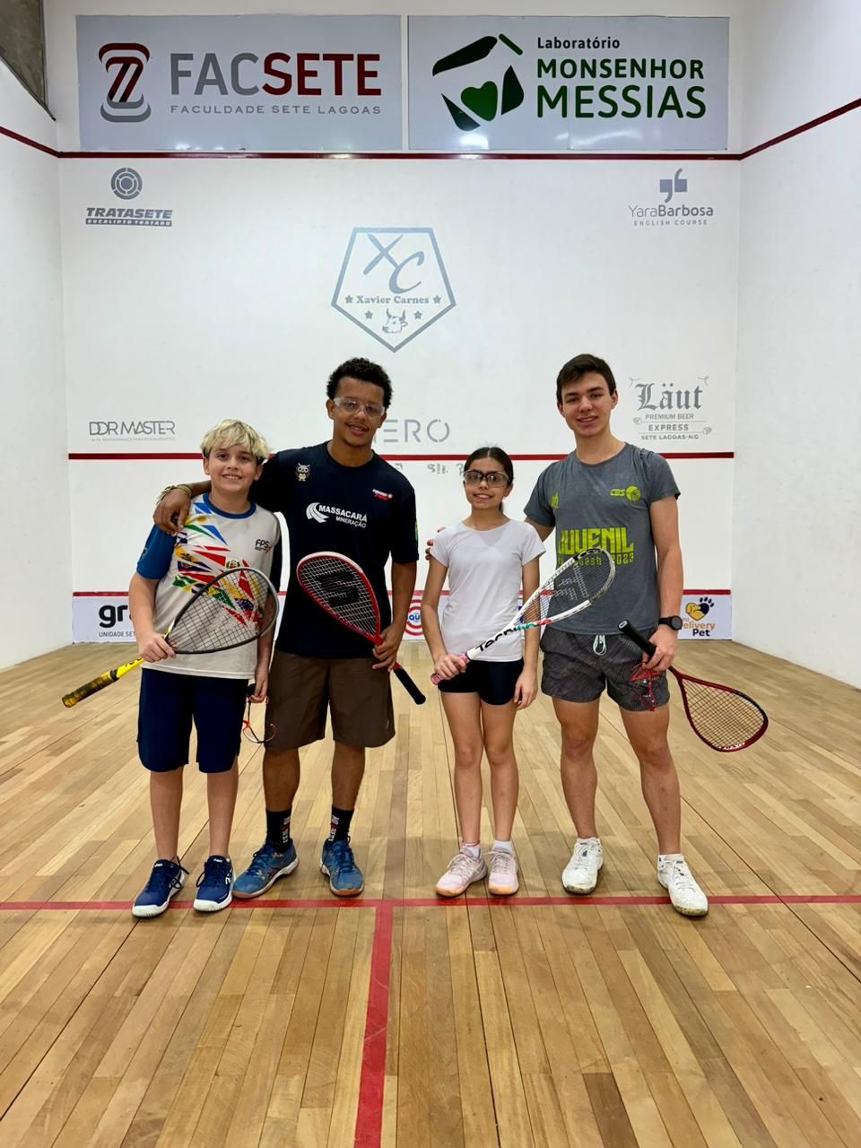 Um grupo de jovens está posando para uma foto em uma quadra de squash.