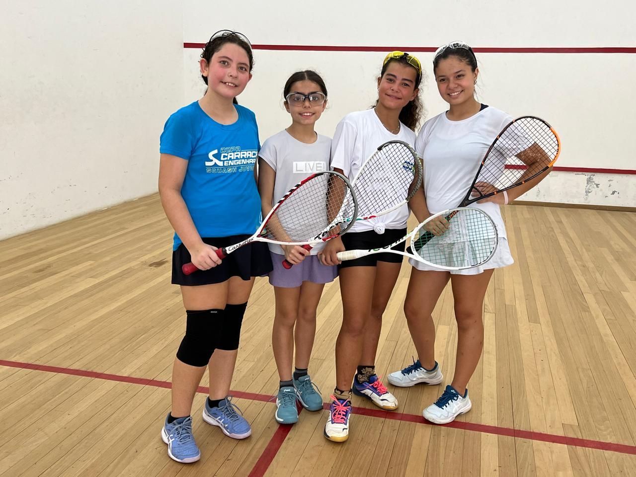 Um grupo de jovens garotas está posando para uma foto em uma quadra de squash