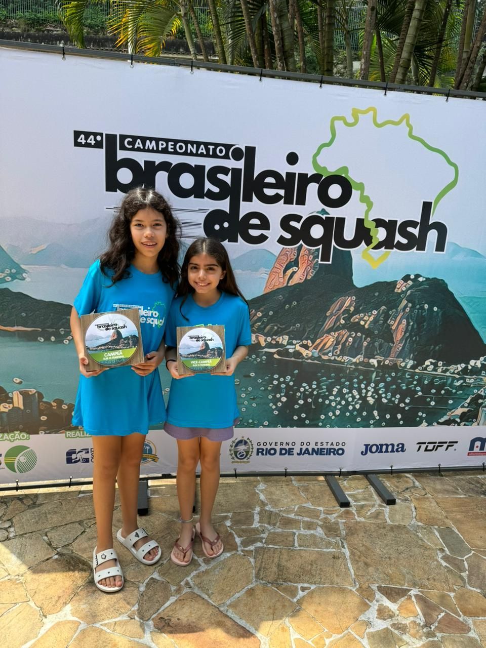 Duas meninas estão em frente a uma placa que diz brasileiro de squash