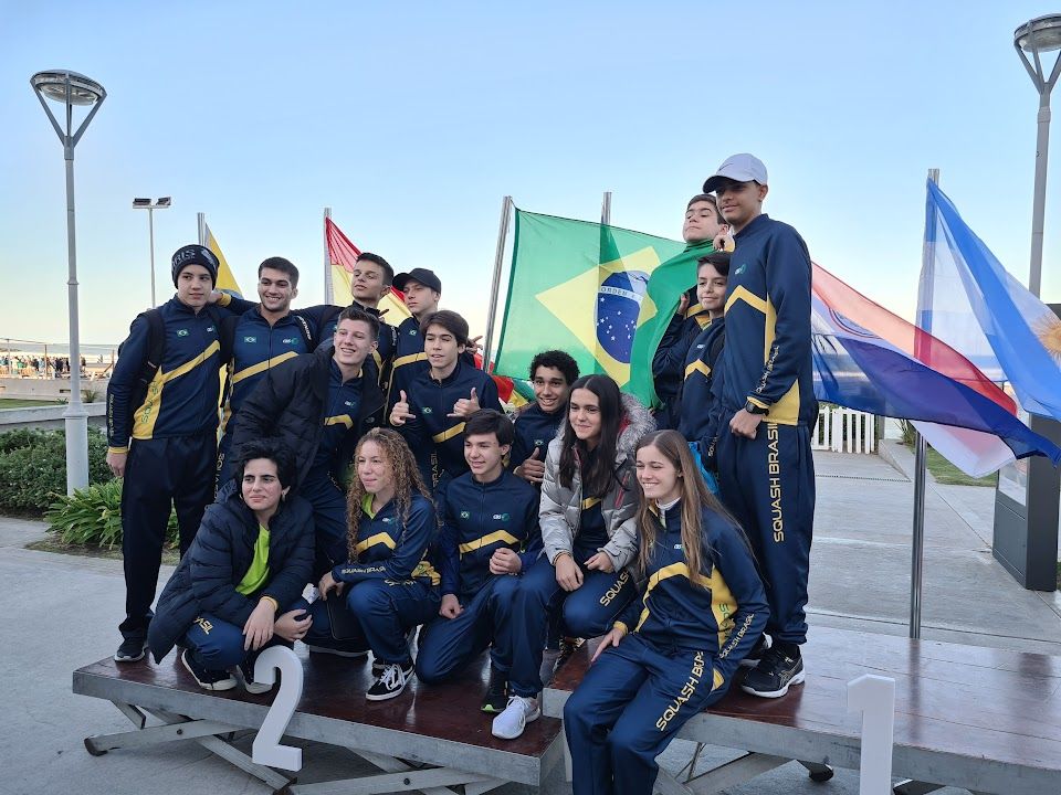 Um grupo de pessoas está posando para uma foto com bandeiras ao fundo.