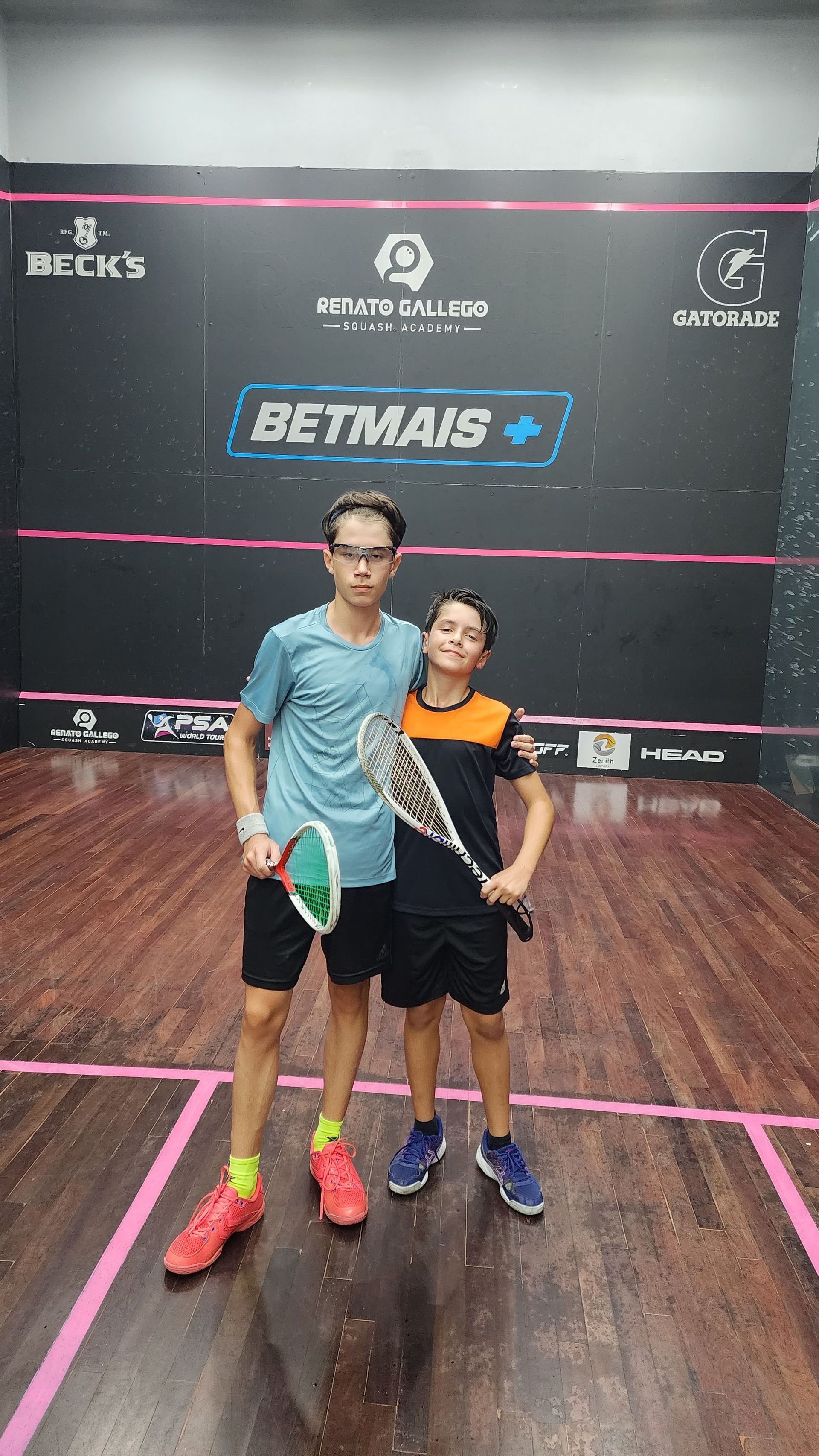 Dois meninos estão posando para uma foto em uma quadra de squash.