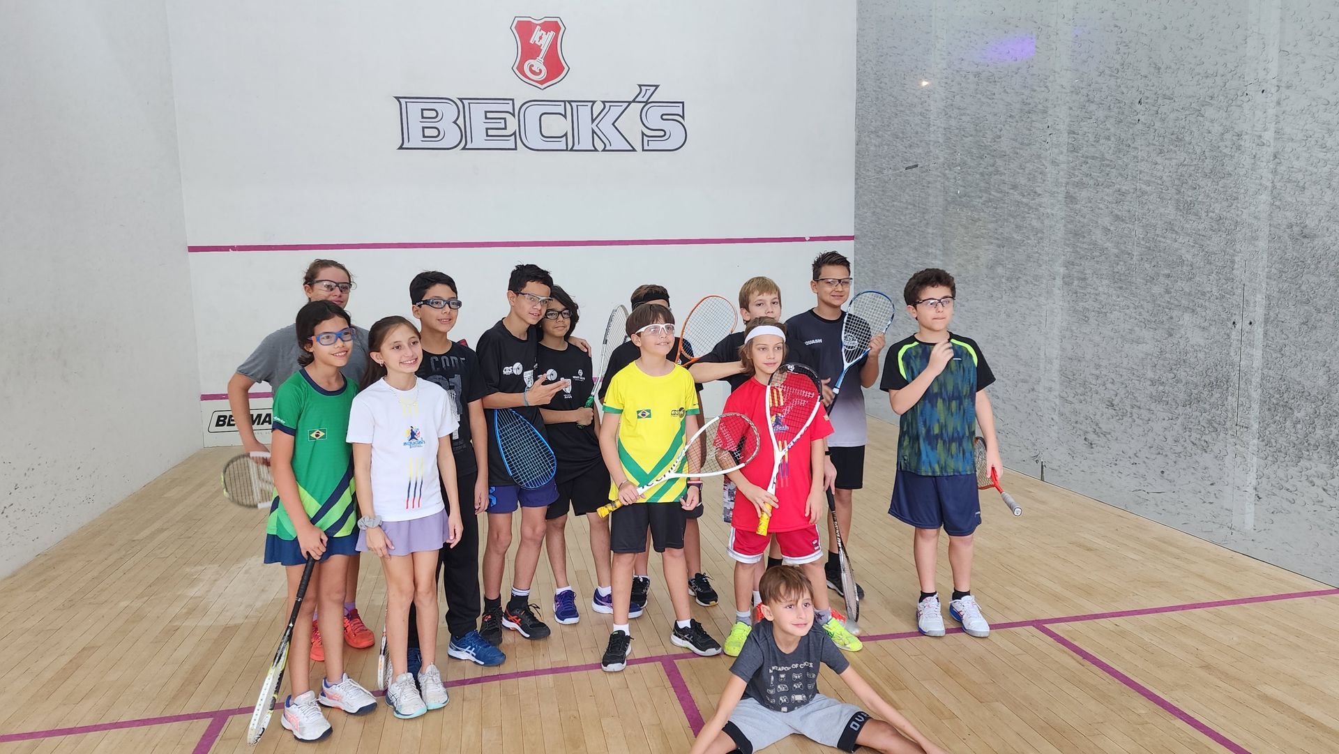 Um grupo de crianças está posando para uma foto em uma quadra de squash.