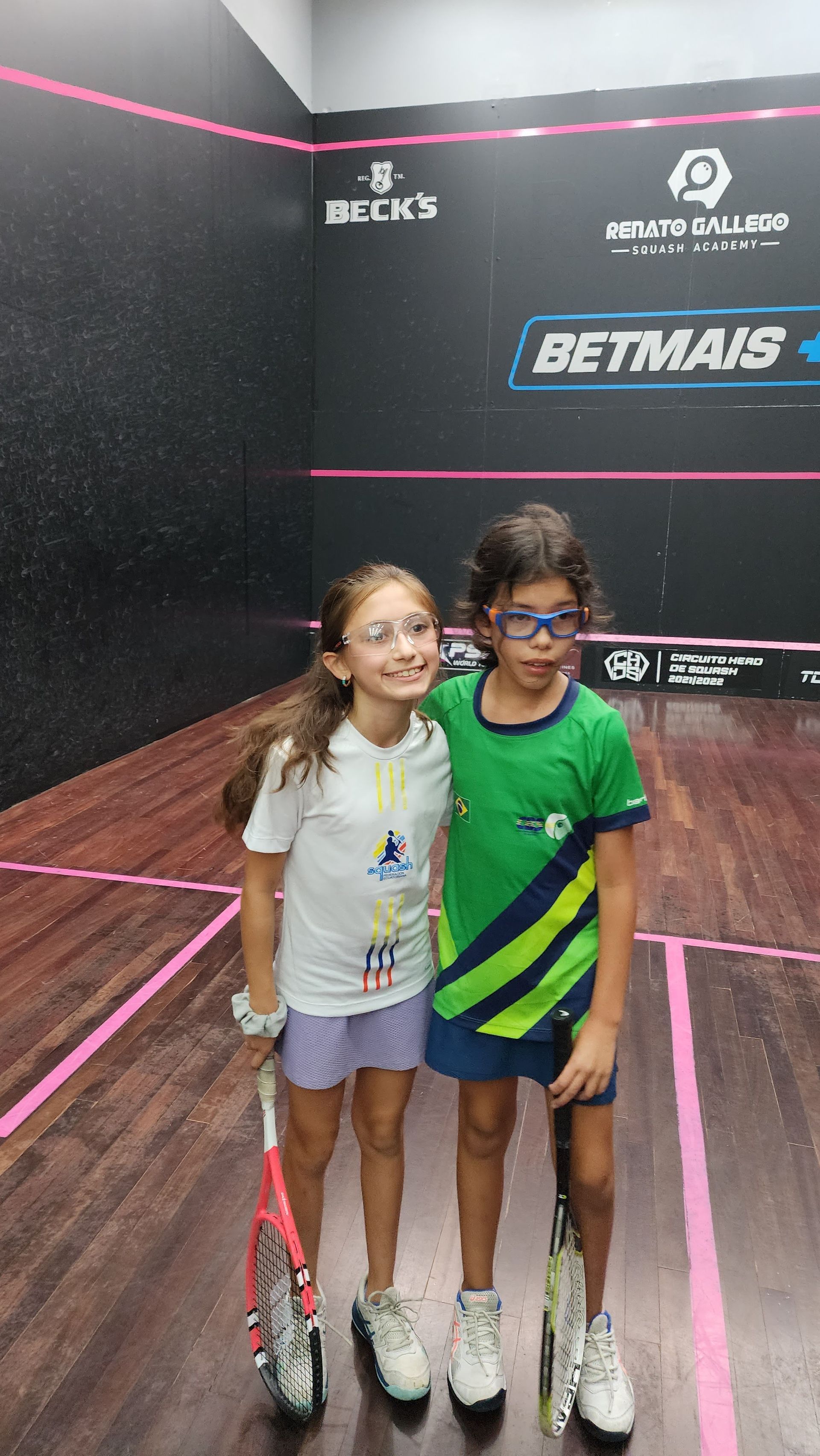 Duas jovens estão posando para uma foto em uma quadra de squash.