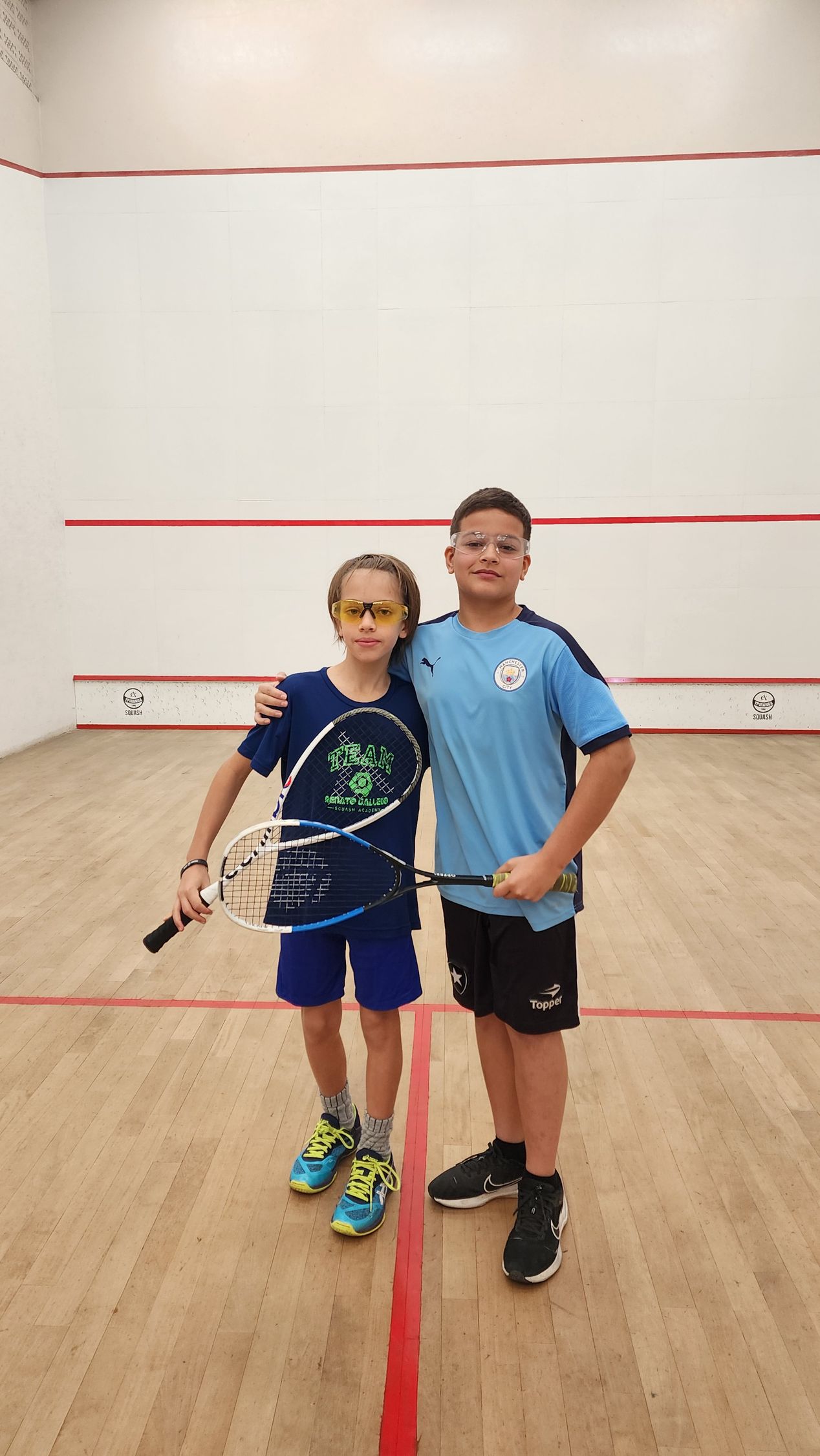 Dois meninos estão posando para uma foto em uma quadra de squash