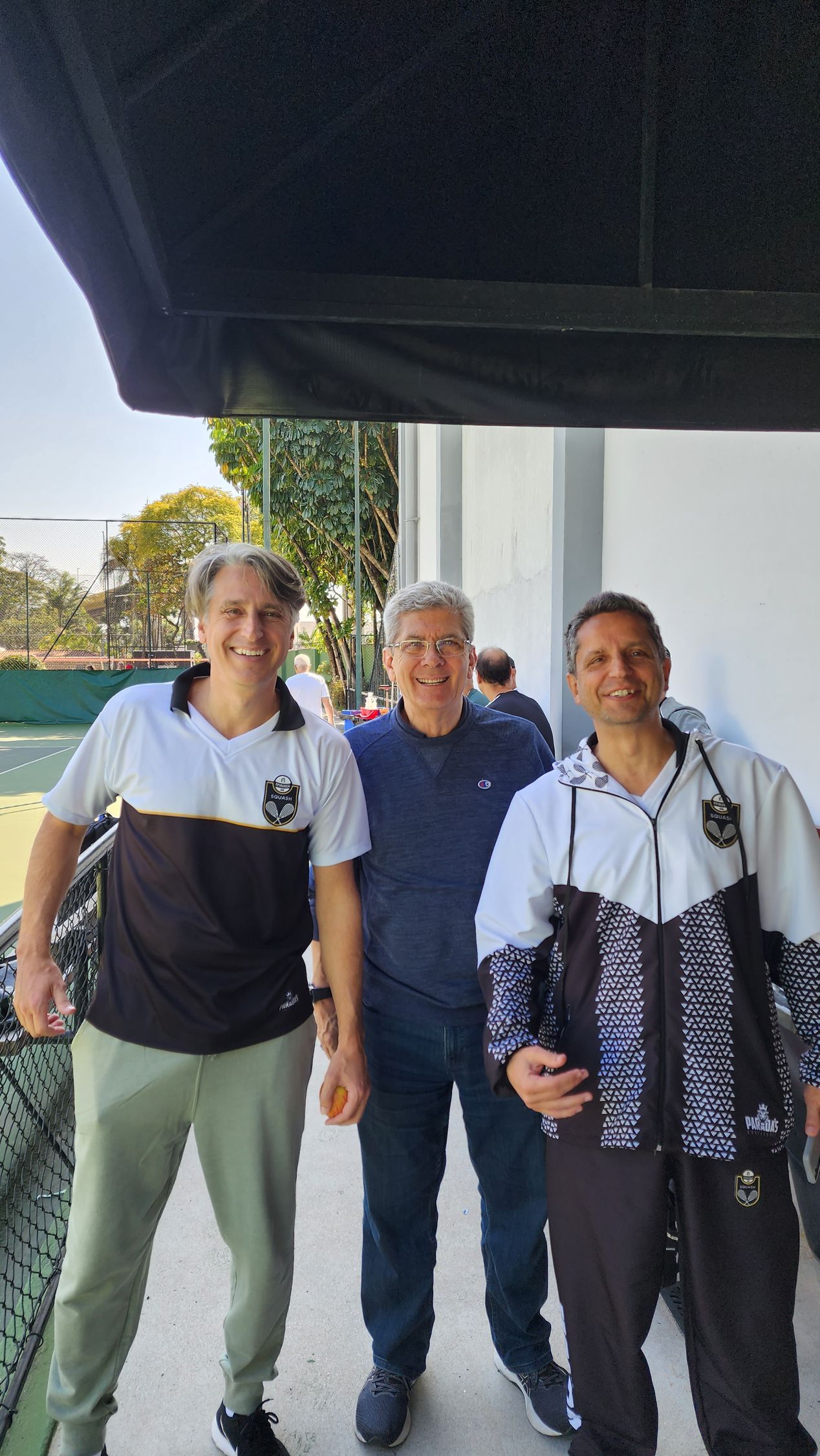 Três homens estão parados um ao lado do outro em frente a um prédio.