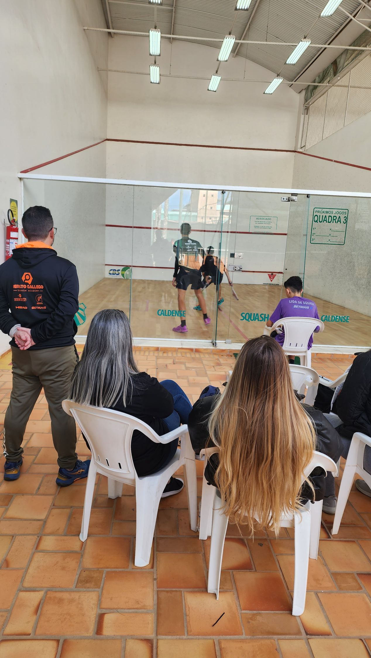 Um grupo de pessoas está sentado em cadeiras assistindo a um jogo de squash.