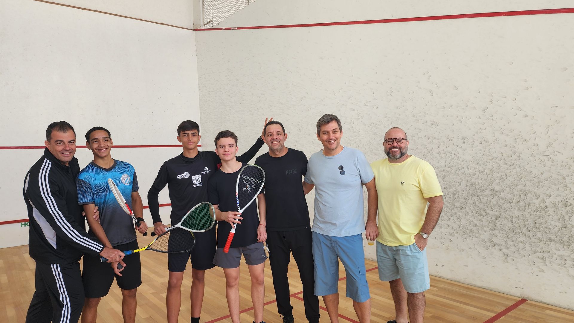 Um grupo de homens está posando para uma foto em uma quadra de squash.
