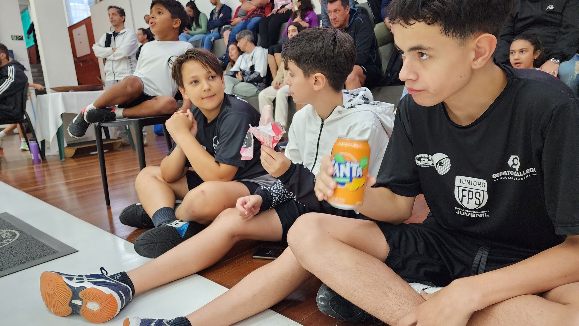 Um grupo de meninos está sentado no chão comendo sorvete e bebendo fanta.