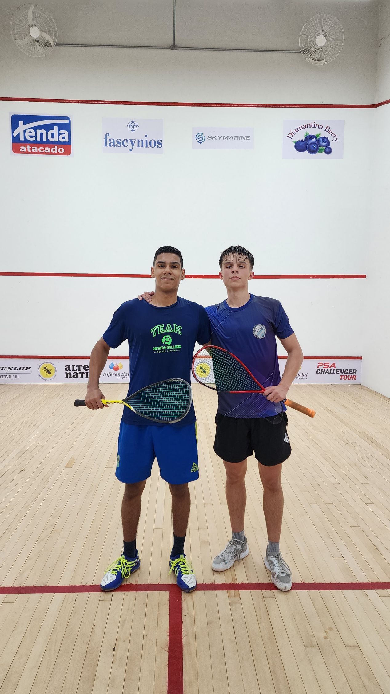 dois homens estão um ao lado do outro em uma quadra de squash segurando raquetes.