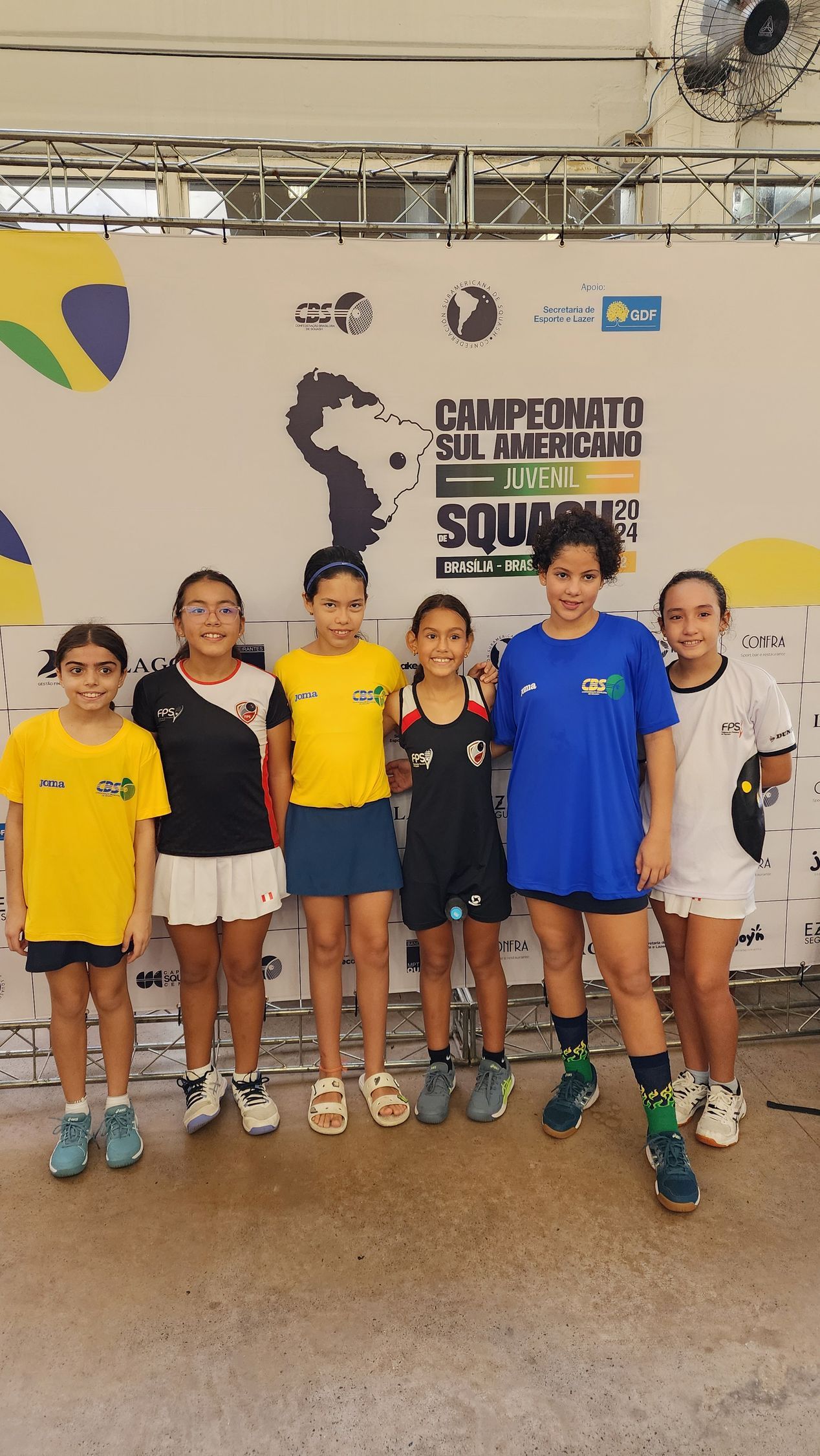 um grupo de meninas posa para uma foto em frente a uma parede que diz 'esporte'